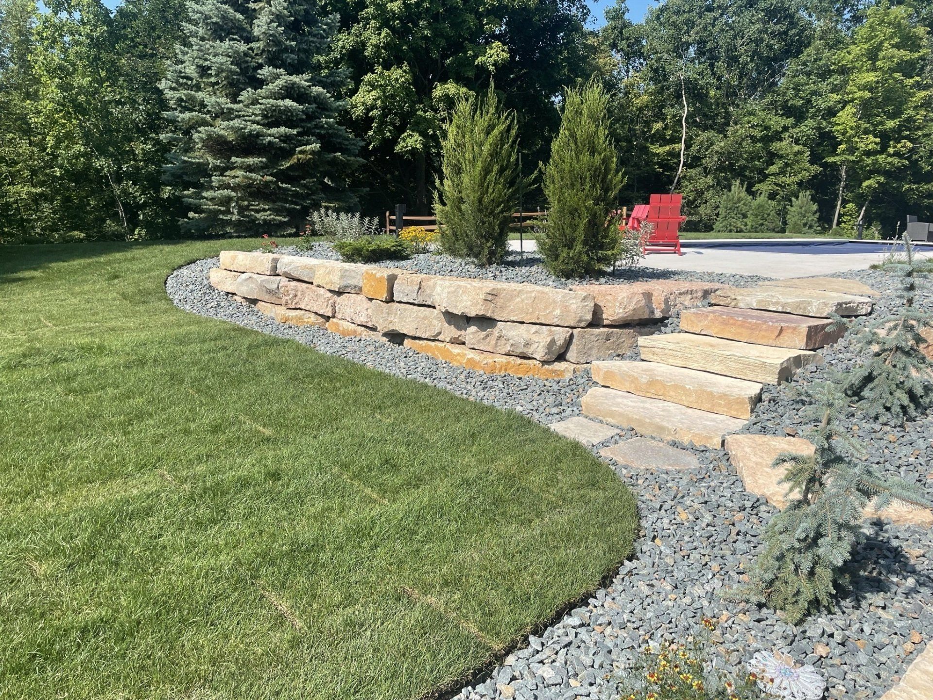 Stone retaining wall and steps with landscaping and green grass.