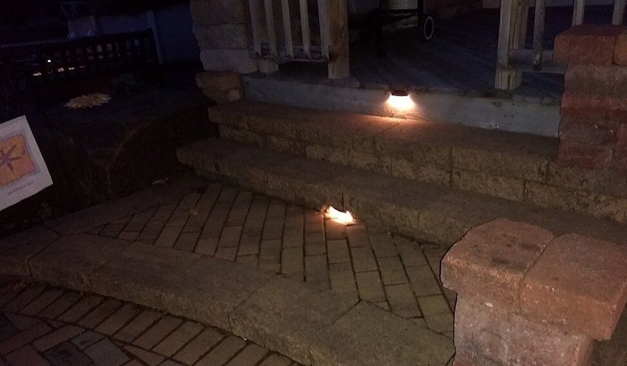 Brick steps and walkway leading up to a porch, illuminated by warm lights at night.