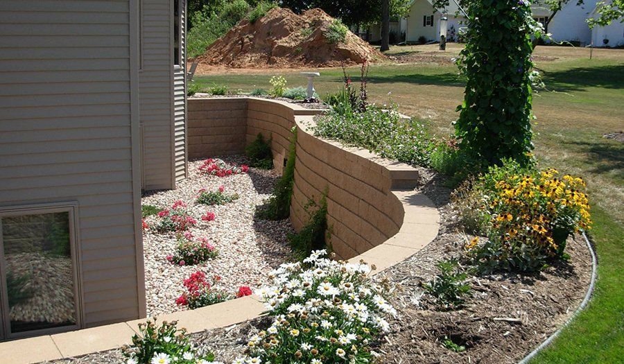 Landscaped backyard with retaining wall, flower beds, and tan siding.