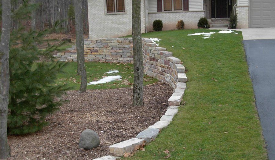 Curved retaining wall with trees and lawn next to a driveway.