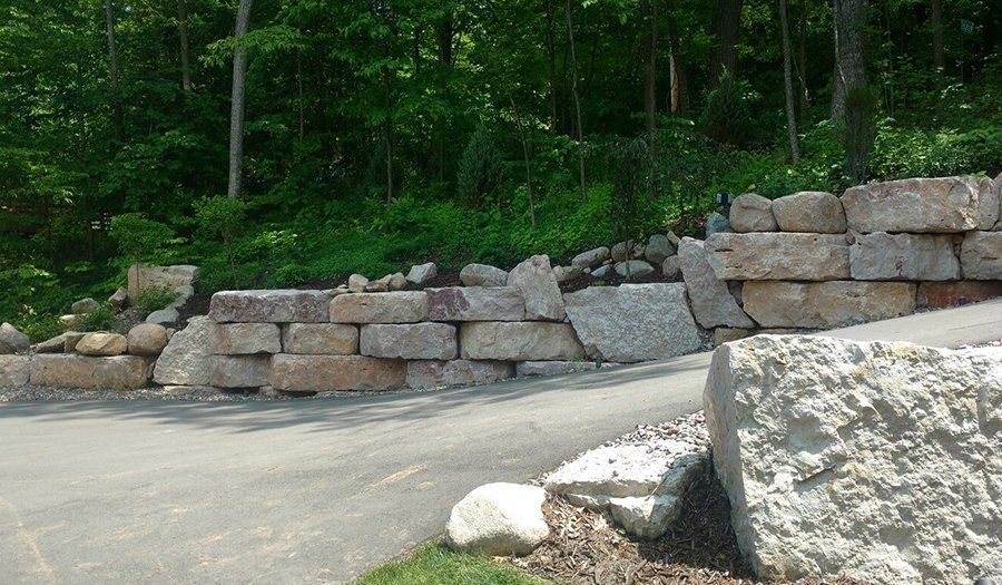 Granite block retaining wall beside a paved driveway, with green trees in the background.