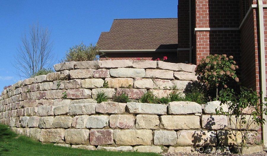 Stone retaining wall in front of a brick building on a sunny day.