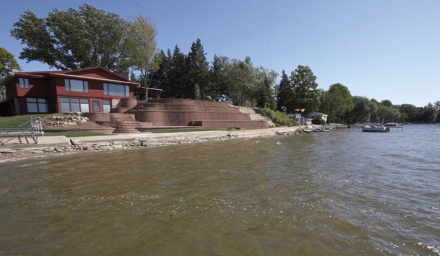 Red house on a lake with a terraced landscape. Boats in water under a blue sky.