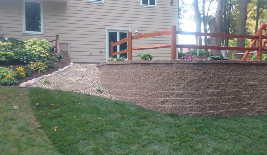 A backyard with a retaining wall, lawn, wooden fence, and house with a sliding glass door.