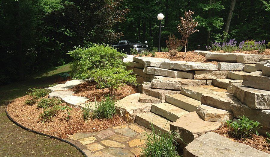 Stone steps and retaining walls in a landscaped garden with mulch and various plants.