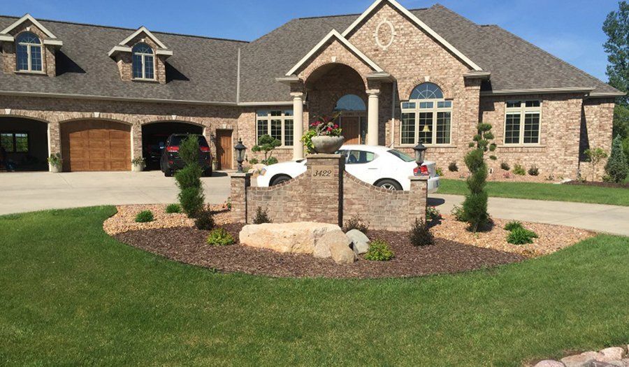 Large brick house with attached garage, landscaped yard, and two cars parked in the driveway.