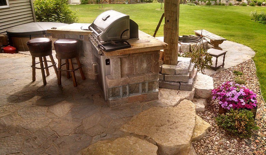Outdoor kitchen with grill, seating, and stone accents.