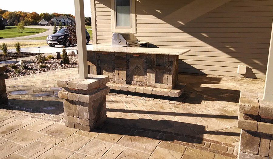 Outdoor kitchen with stone bar and built-in grill under a covered patio.