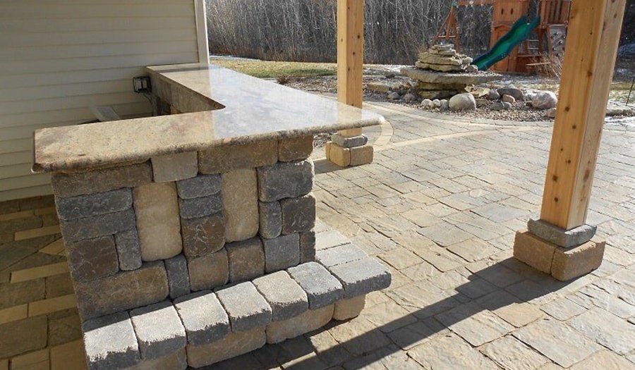 Outdoor stone bar with granite countertop, built on a patio, with wooden posts and a playset in the background.