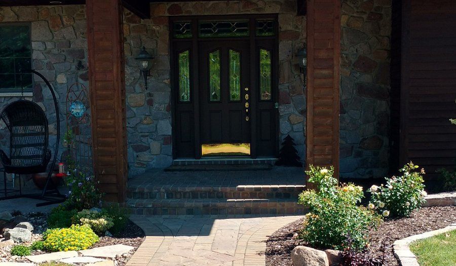 Front entrance of a house with stone and wood exterior. Brown door, walkway, and landscaping.