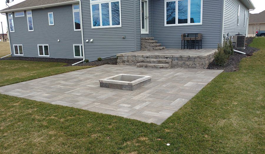 Backyard patio with fire pit, raised stone wall, gray home with steps.