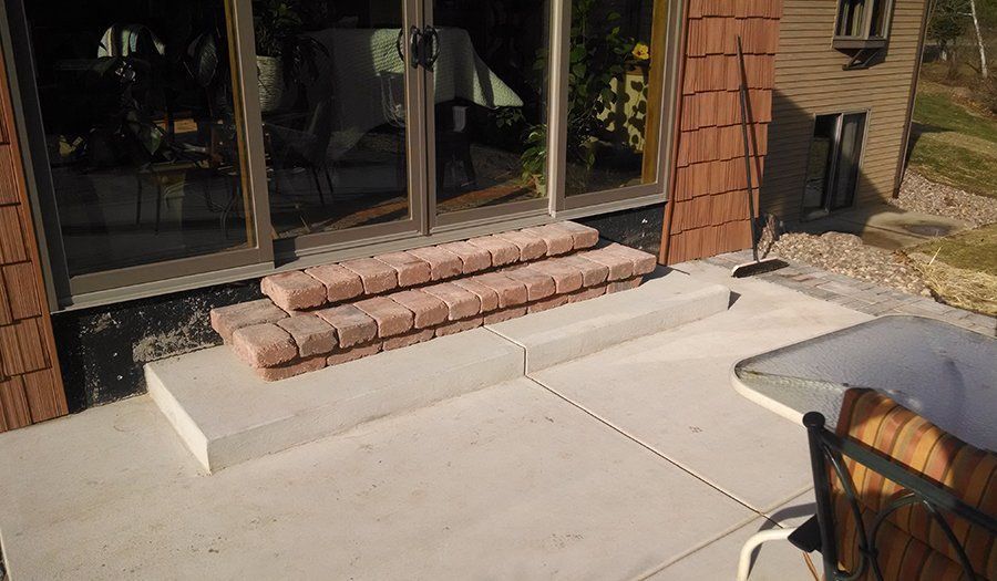 Exterior concrete steps with brick edging, leading to glass doors, alongside a patio.