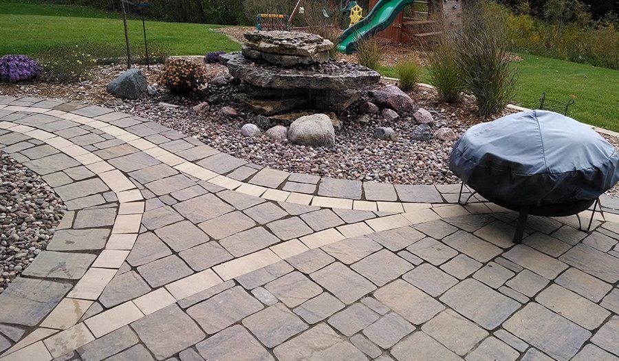 Stone patio with fire pit, water feature, and a child’s playground in the background.