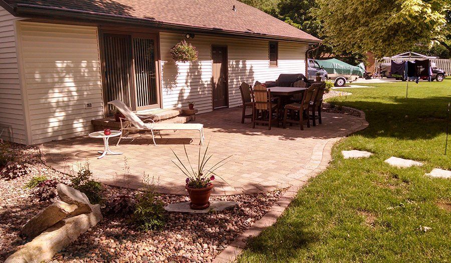 Brick patio with outdoor furniture next to a house and lawn.