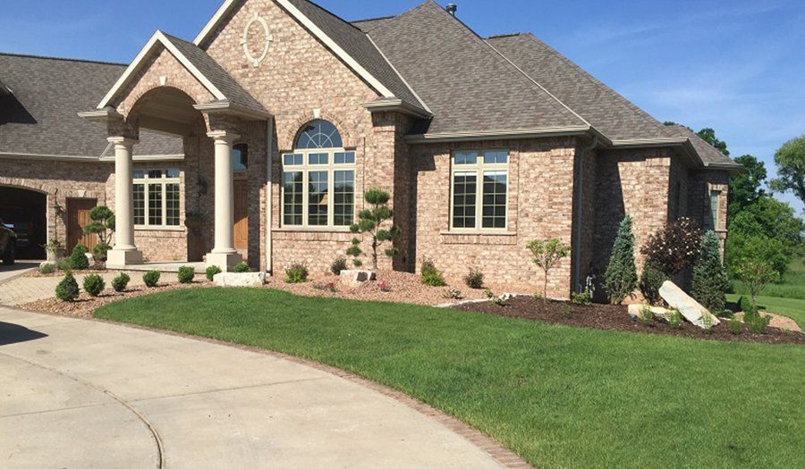 Brick house with manicured lawn, driveway, and landscaping on a sunny day.