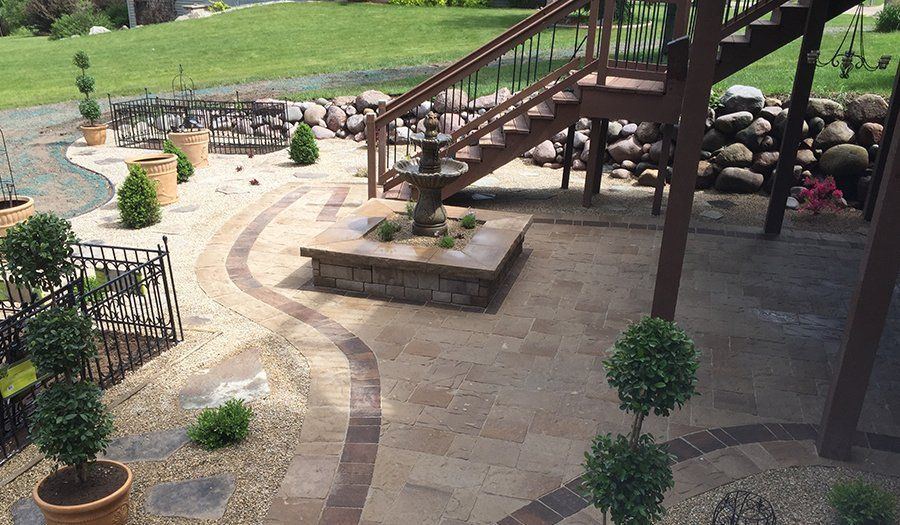 Backyard patio with stone walkway, fountain, steps, and greenery.