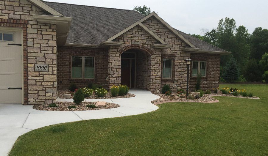 House with brick and stone facade, arched entryway, and landscaped front yard with a curved walkway.