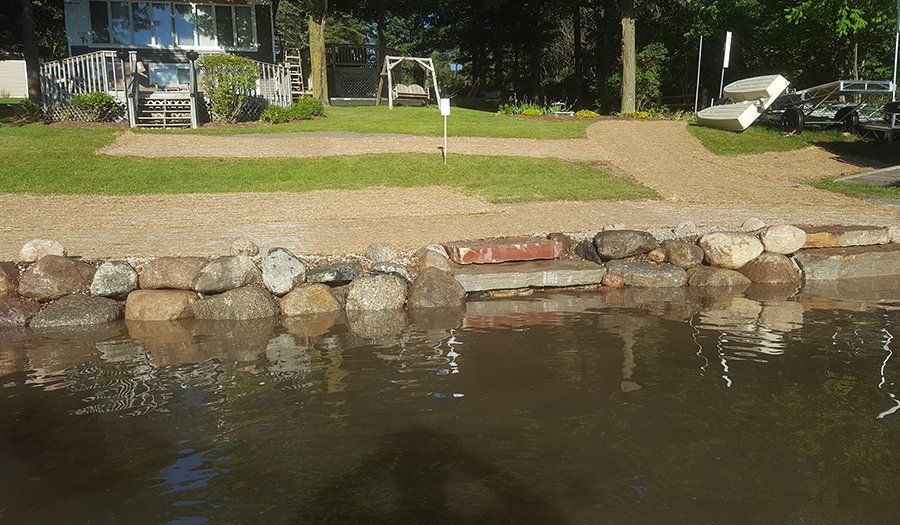 Lakefront property with a stone retaining wall and grass leading to the water.
