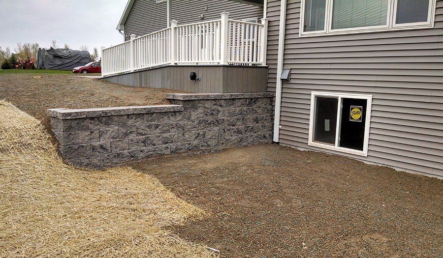 Gray retaining wall next to a house with a deck. The ground is covered with gravel.