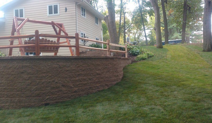 Backyard with retaining wall, wooden swing, and sloped green lawn. House in the background.