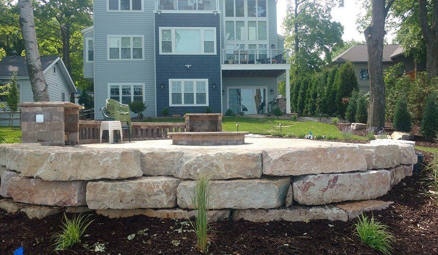 Stone retaining wall with a fire pit area in front of a multi-story house.