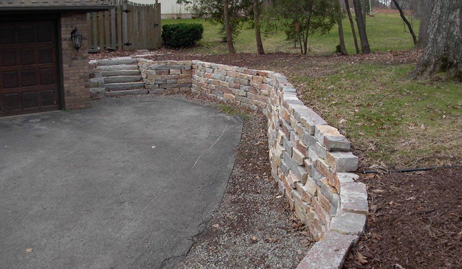 Stone retaining wall curving along a driveway, with steps leading up from it.