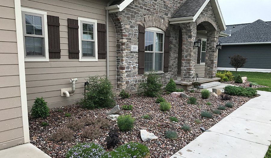 House exterior with stone and siding, landscaped rock bed, and a concrete walkway.