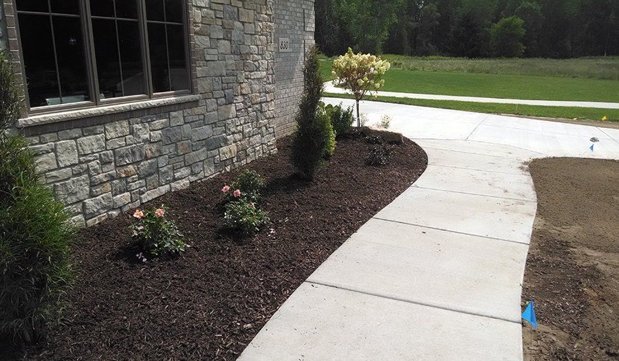 Stone house exterior with a mulched garden bed and a concrete walkway.