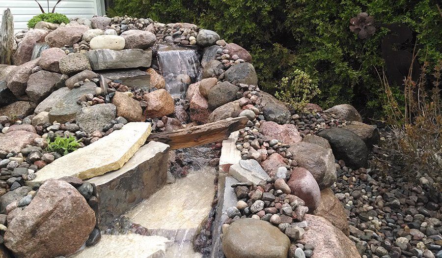 Rock waterfall with cascading water, surrounded by rocks and pebbles.