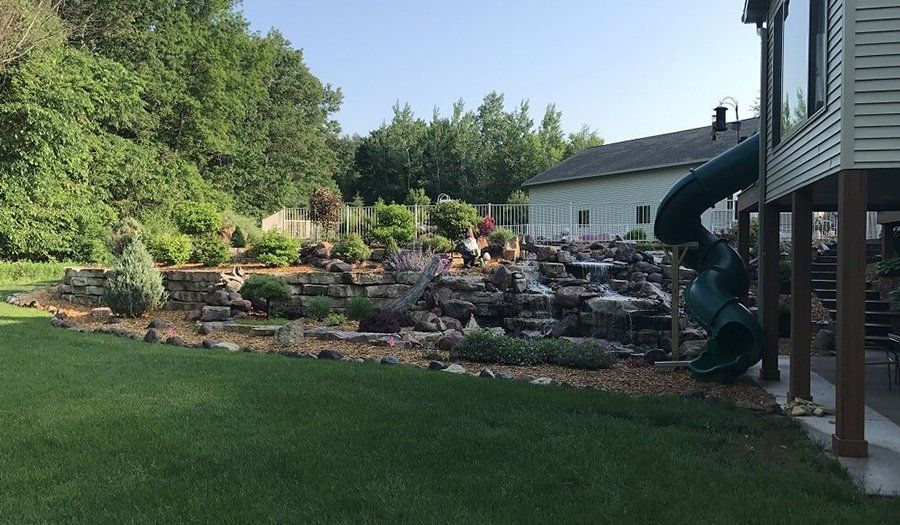 Backyard with a rock waterfall feature, a green slide, and a grassy lawn.
