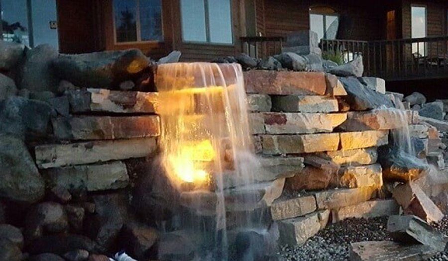 Waterfall feature with stone wall and amber lighting. Water cascades down.