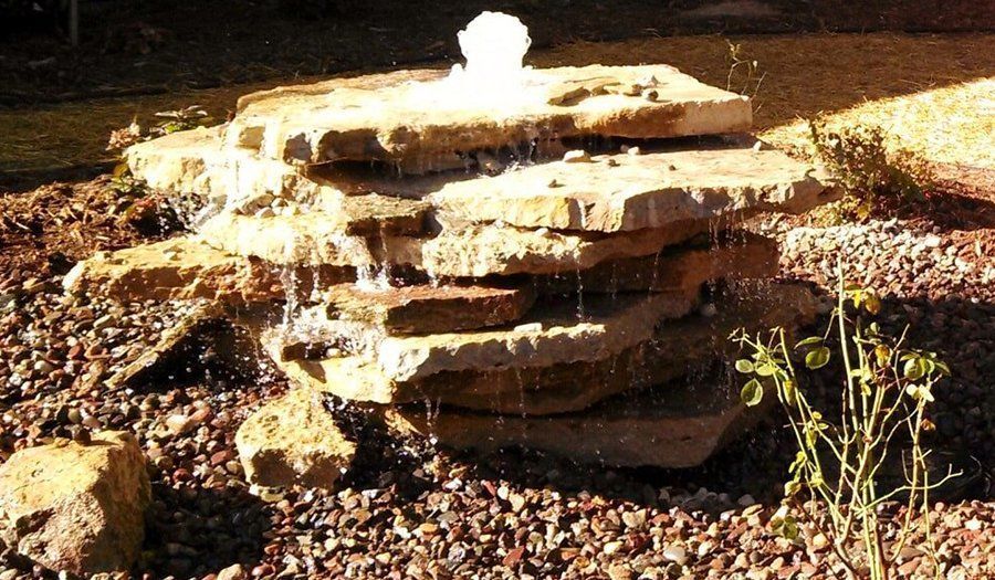 Water fountain made of stacked, flat stones, water cascading down, surrounded by brown rocks.