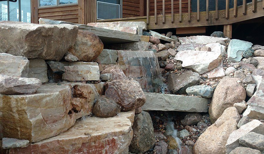 Water cascading down a rock waterfall next to a wooden deck and building.
