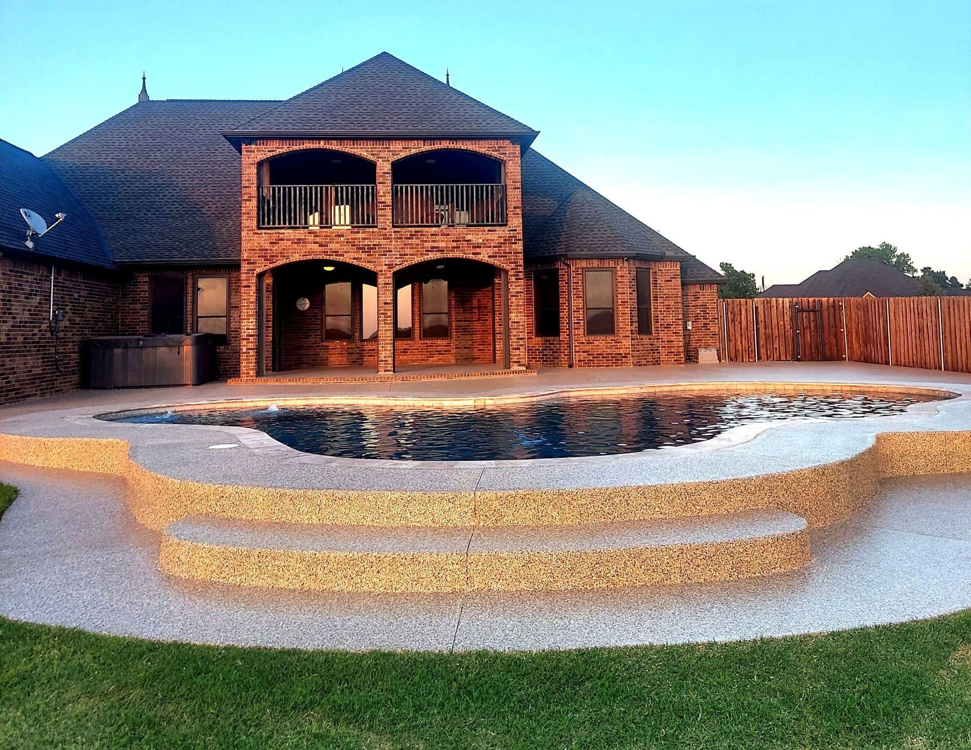 Backyard with pool and steps, brick house, brown roof, and green lawn.