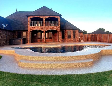 Backyard with pool and steps, brick house, brown roof, and green lawn.