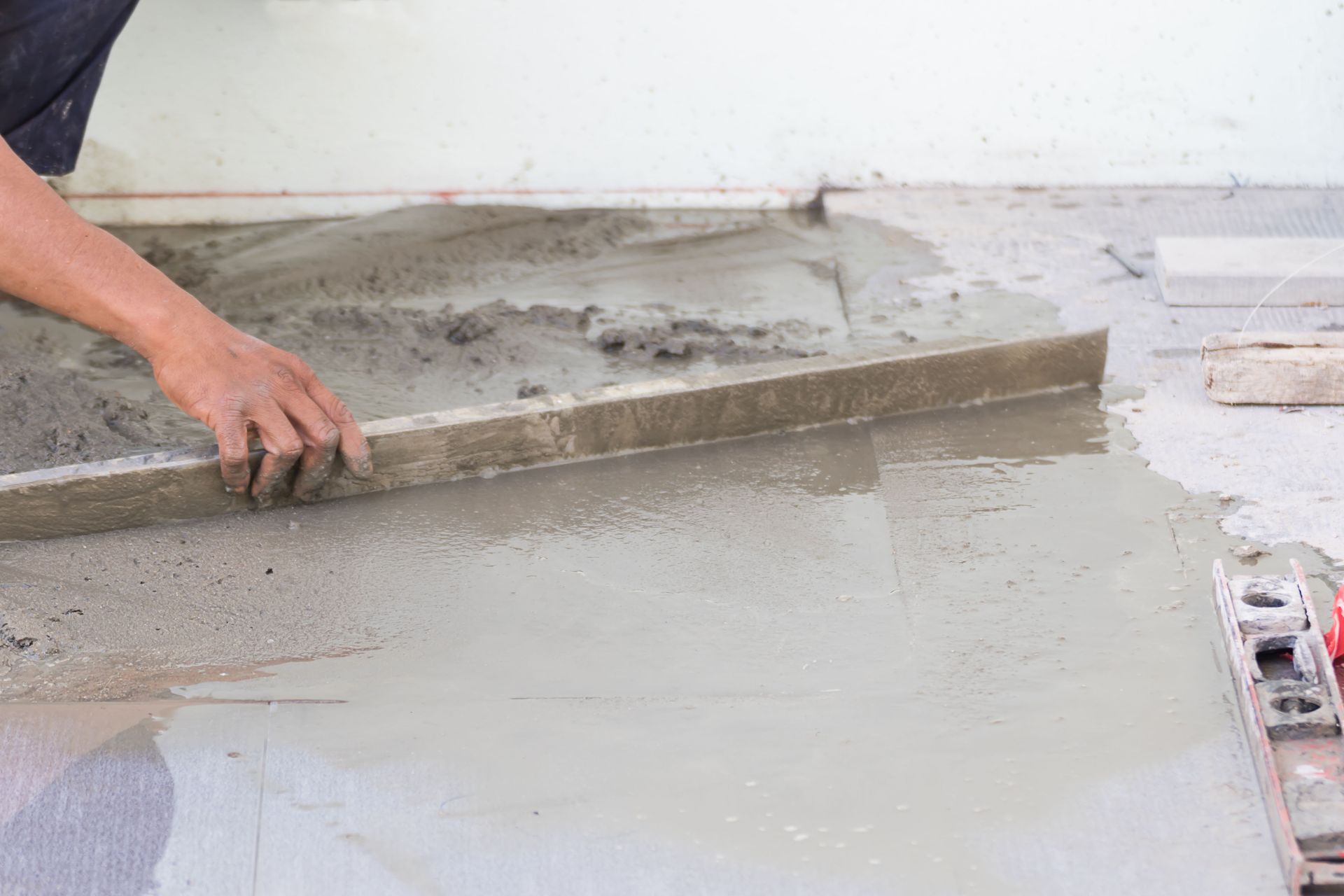 Person using a level to smooth wet cement on a floor, preparing for tiling.