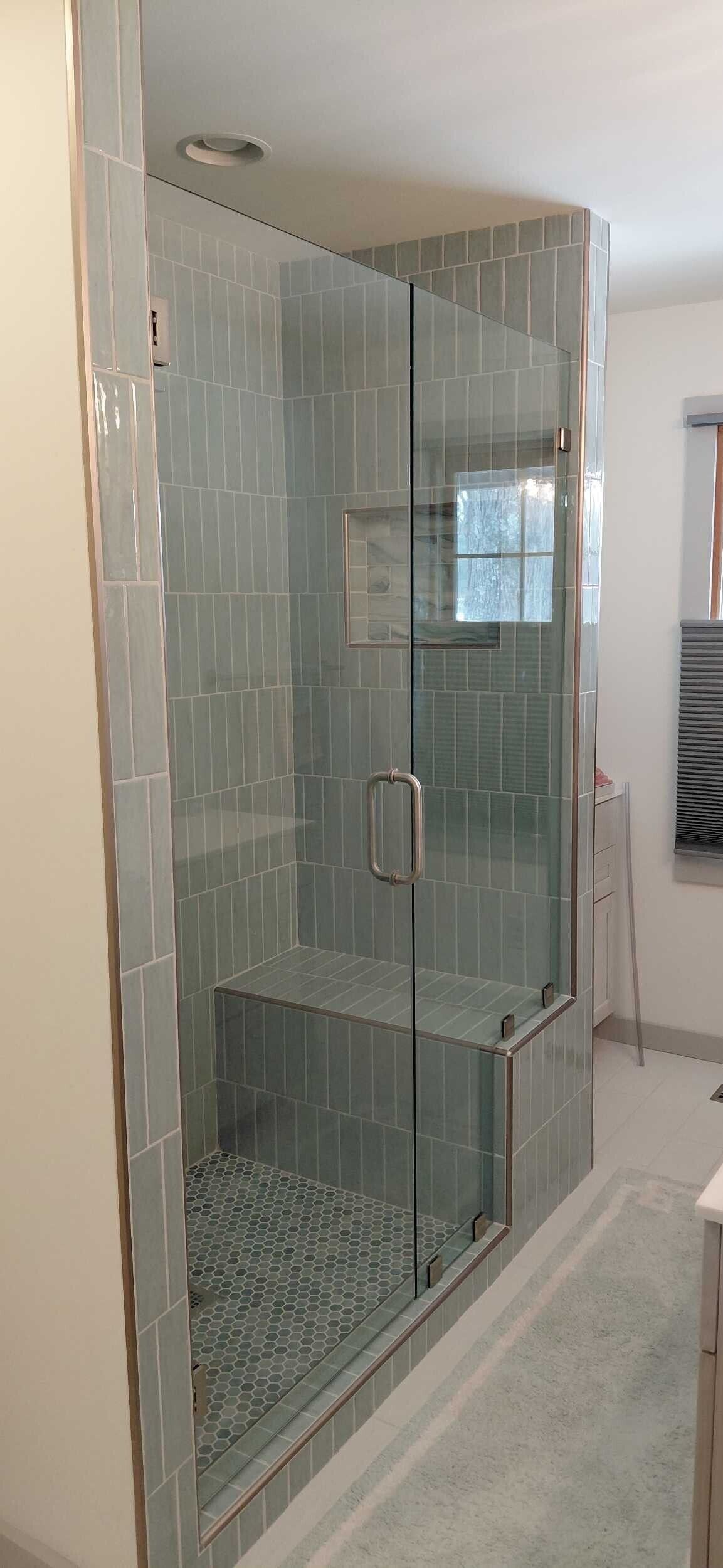 Glass shower enclosure with gray tile and pebble floor.