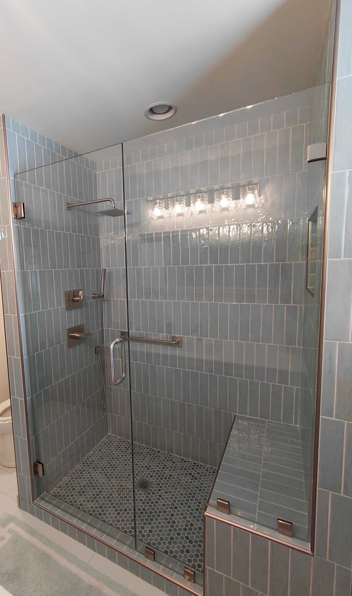 A modern, tiled shower with a glass door and bench. The tiles are teal.