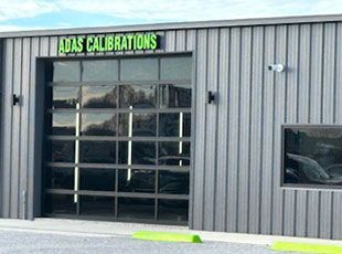 A building with a large garage door and a sign that says ADAS CALIBRATIONS.
