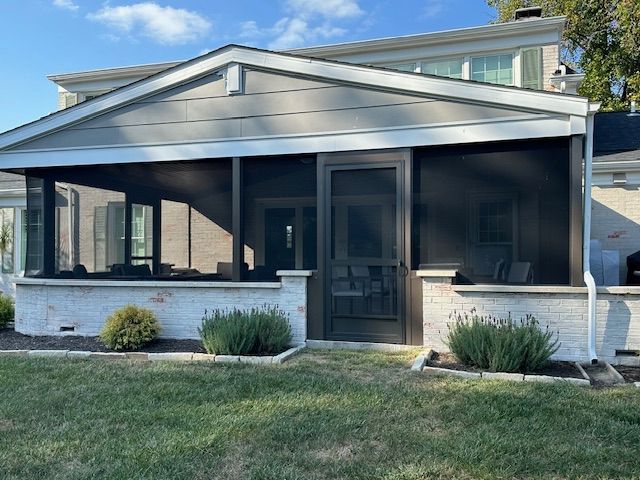 A house with a screened in porch and a large lawn in front of it.