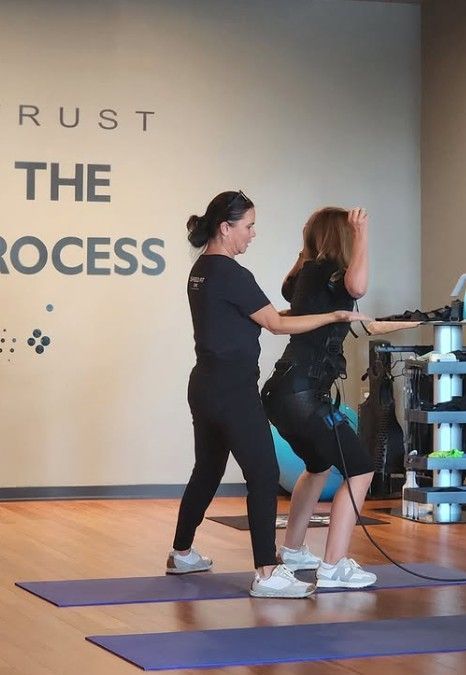 Two women doing seated squats with resistance bands in a studio labeled “The Process”