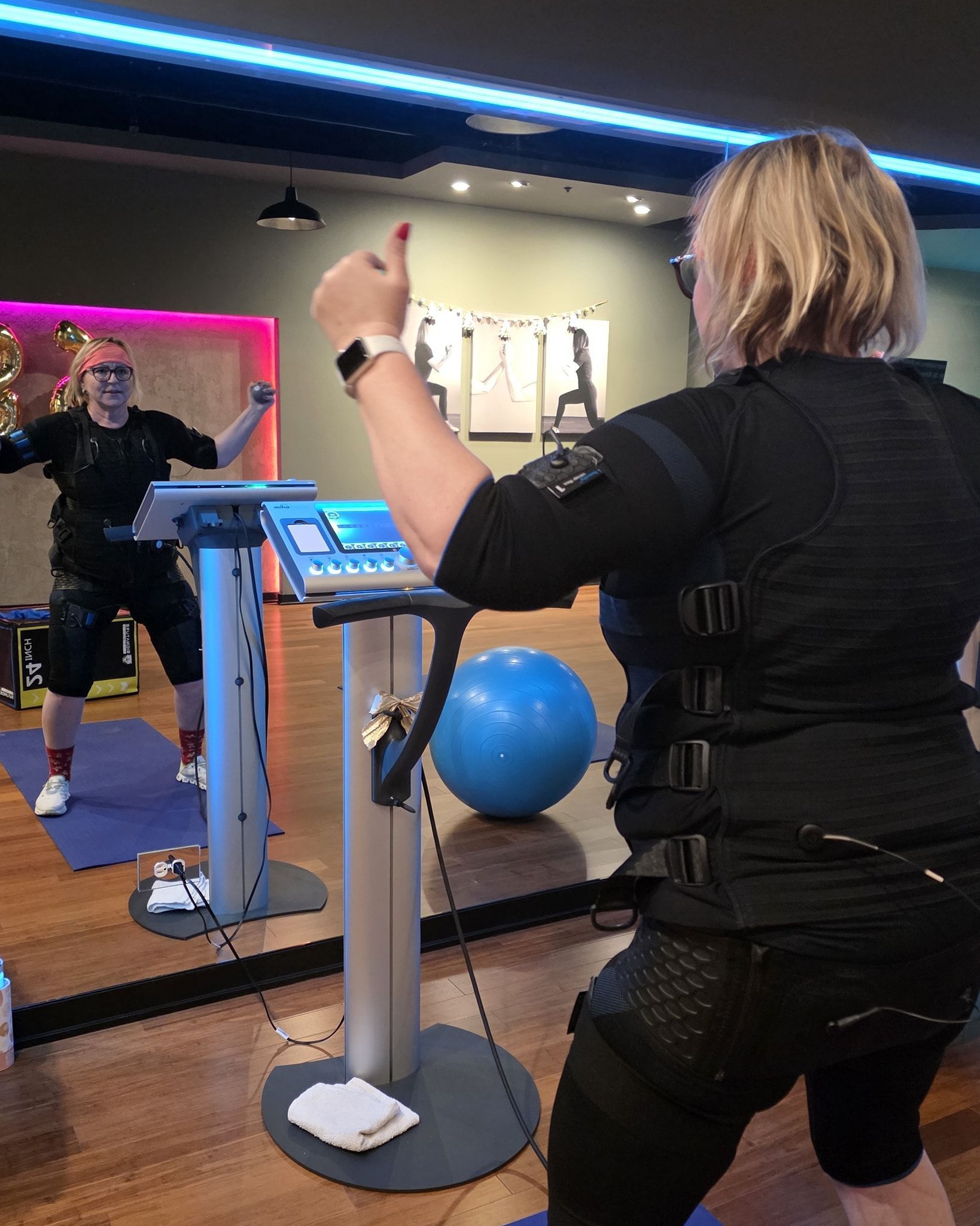 Person exercising on a blue-lit gym machine while watching a mirror, with a blue exercise ball nearby.