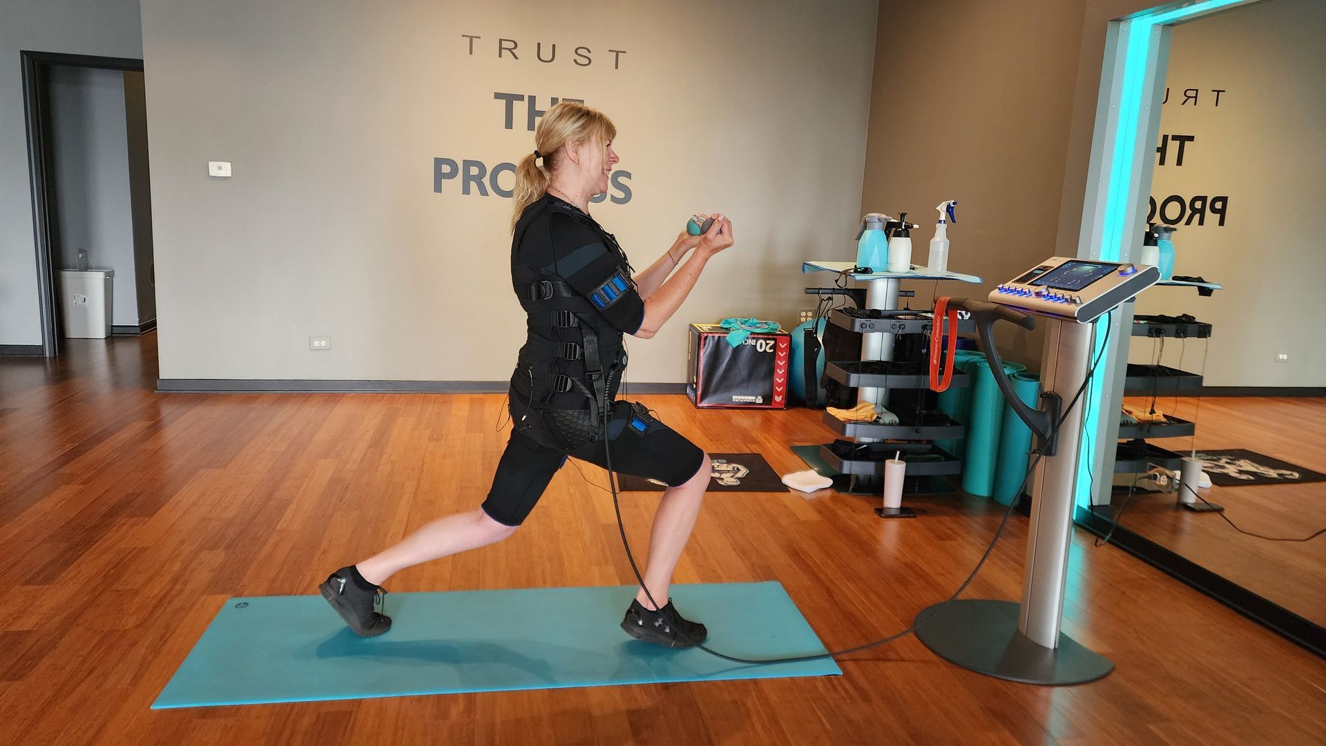 Person lunging on a blue mat in a gym, facing a training machine beside a wall with motivational text.