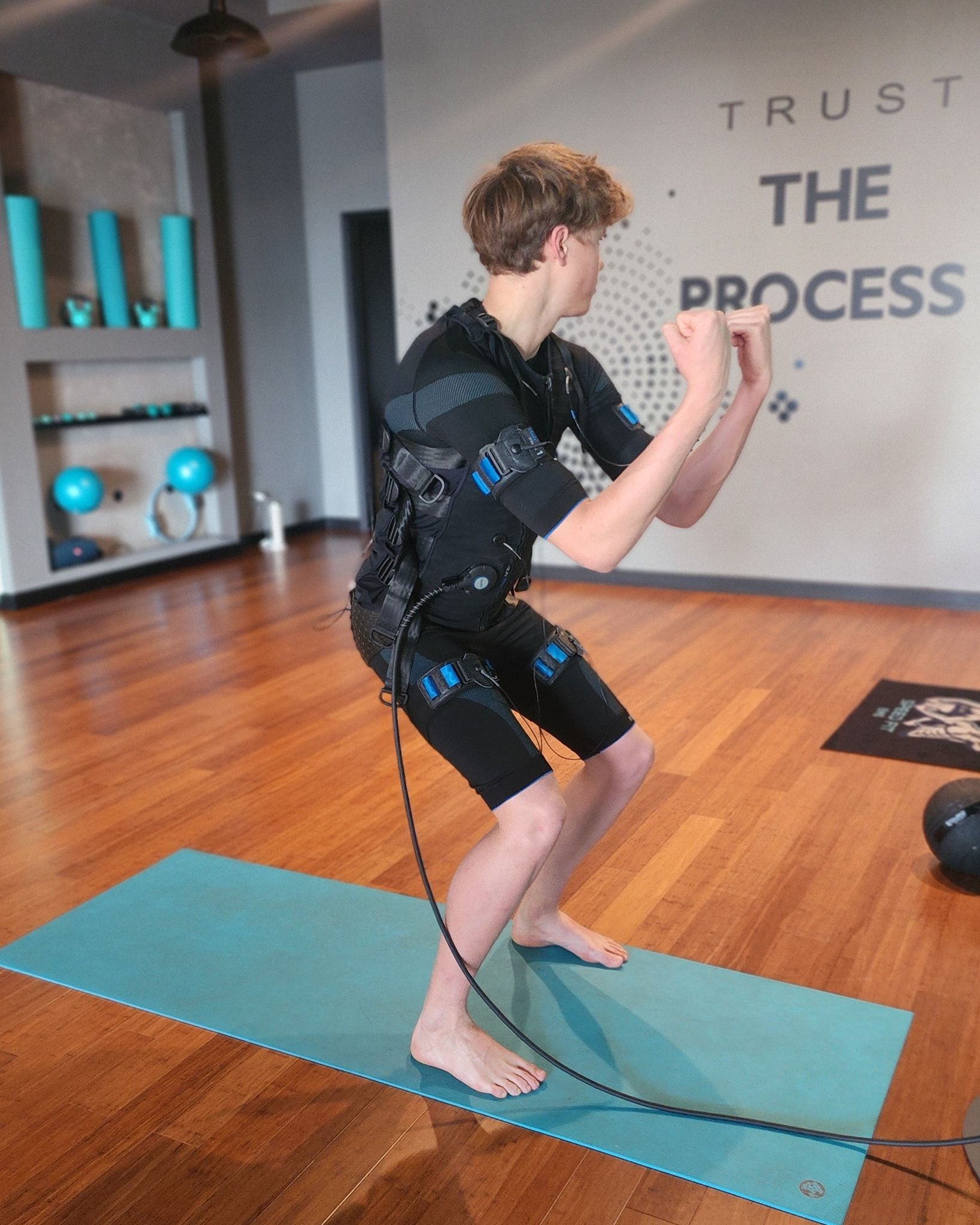 Person doing a squat exercise on a teal mat in a home gym, with “TRUST THE PROCESS” on the wall.
