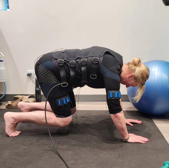 Person kneeling on all fours in a workout suit beside a blue exercise ball in a gym room
