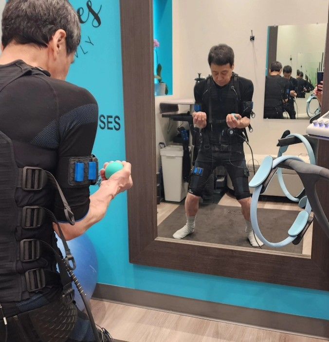 Person in a black EMS suit exercising with EMS gear in front of a mirror at a fitness studio