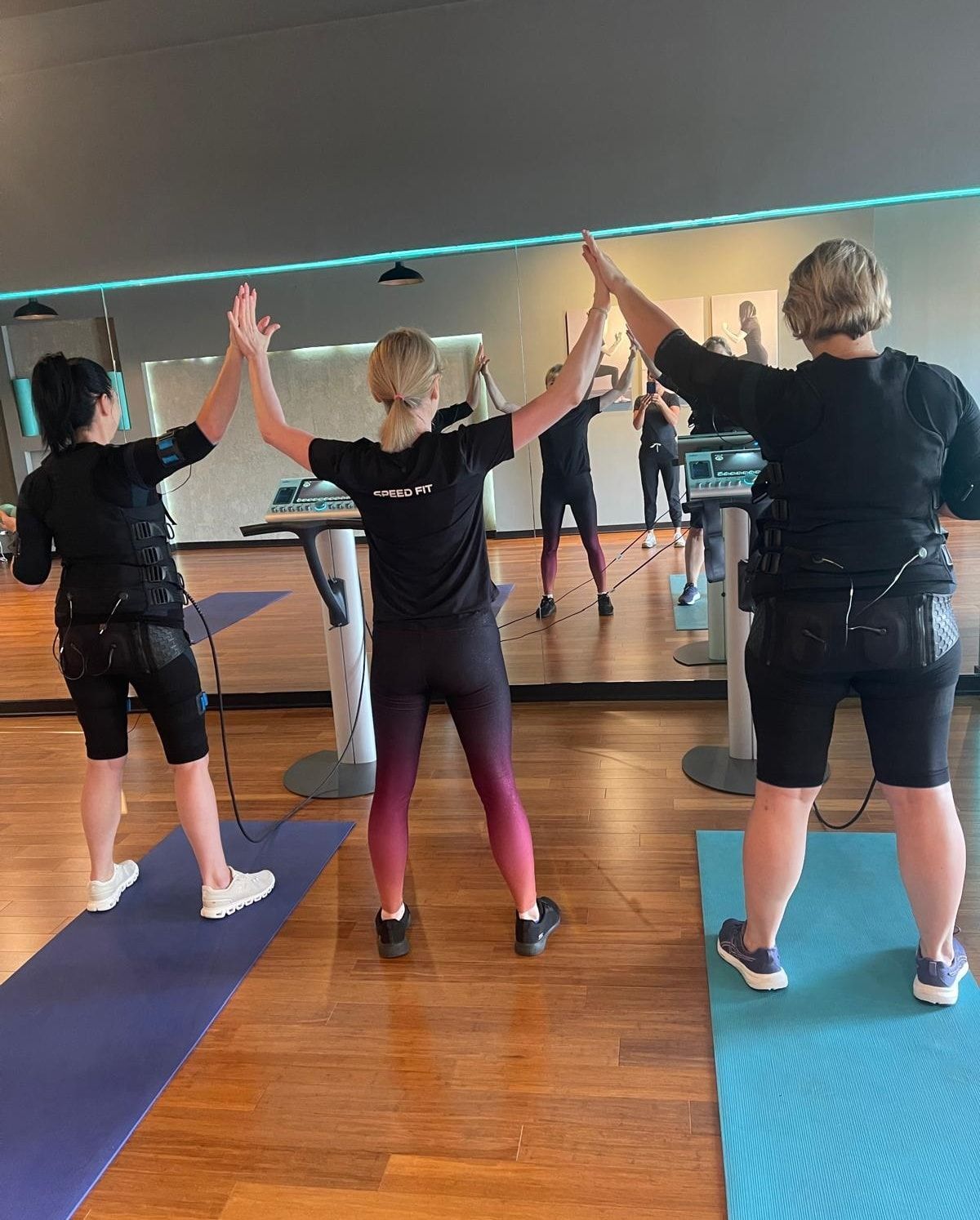 People doing a synchronized workout with arms raised in a mirrored exercise studio