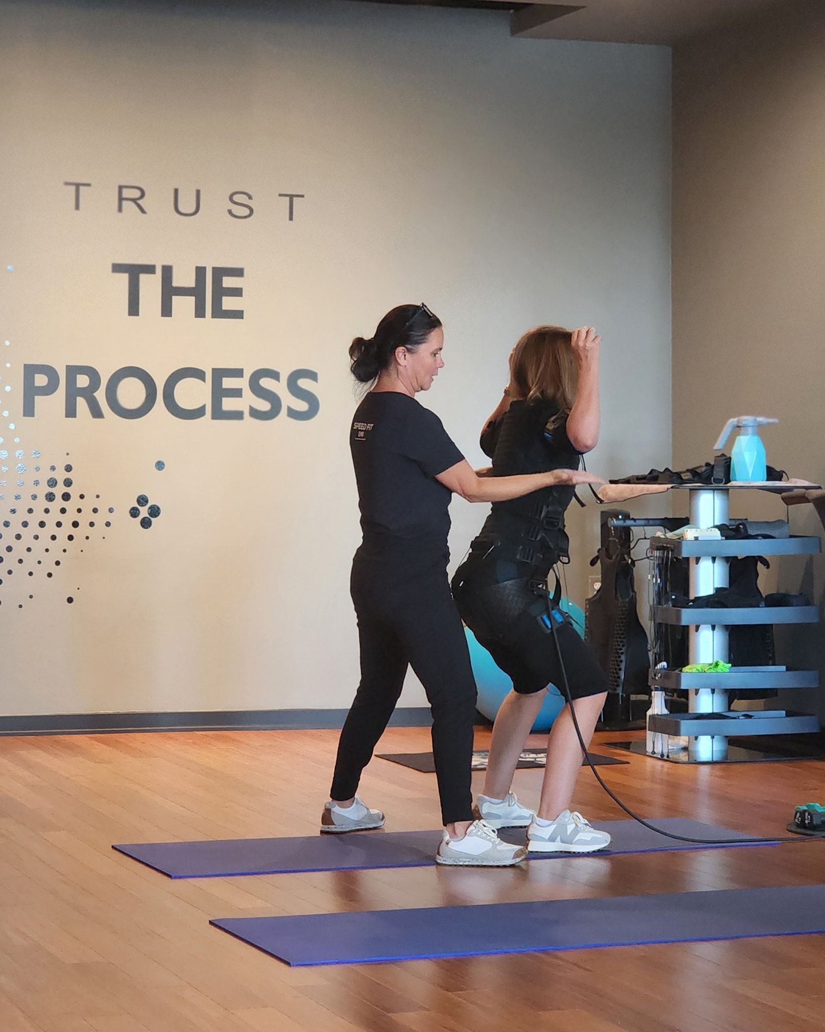 Two people exercising on yoga mats in a gym studio with “TRUST THE PROCESS” on the wall.