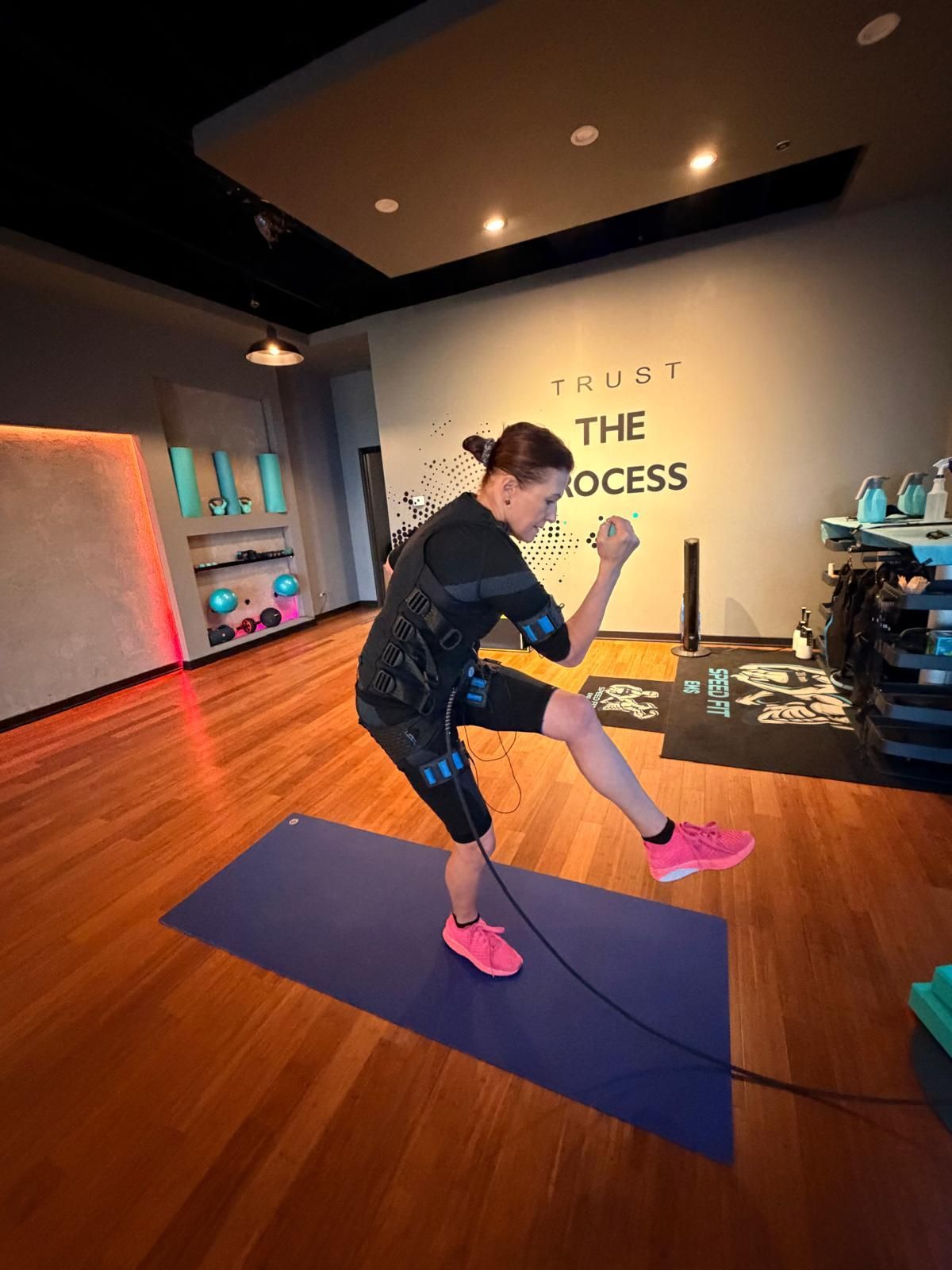 Person stretching on a yoga mat in a studio with wood floors and wall text reading “The Process”