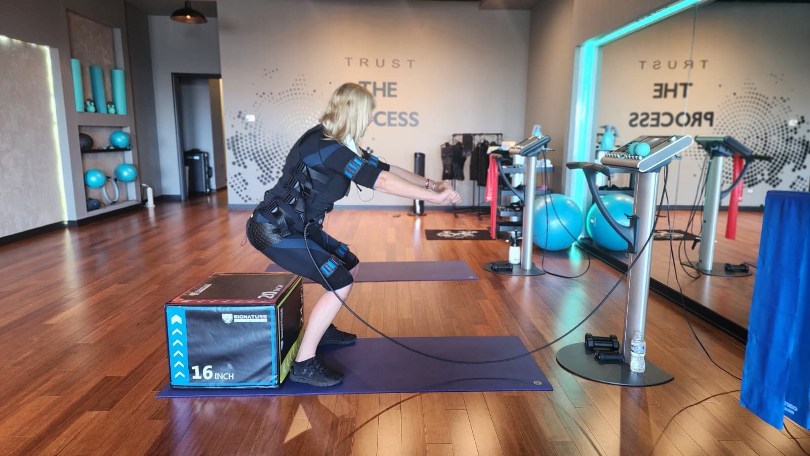 Person squats holding a cable handle in a gym with wood floors and blue-lit equipment.